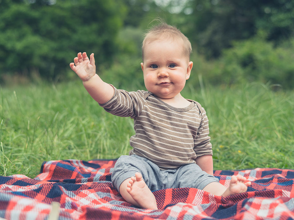 Baby sitting on blanket in grass waving goodbye to torn contact lenses