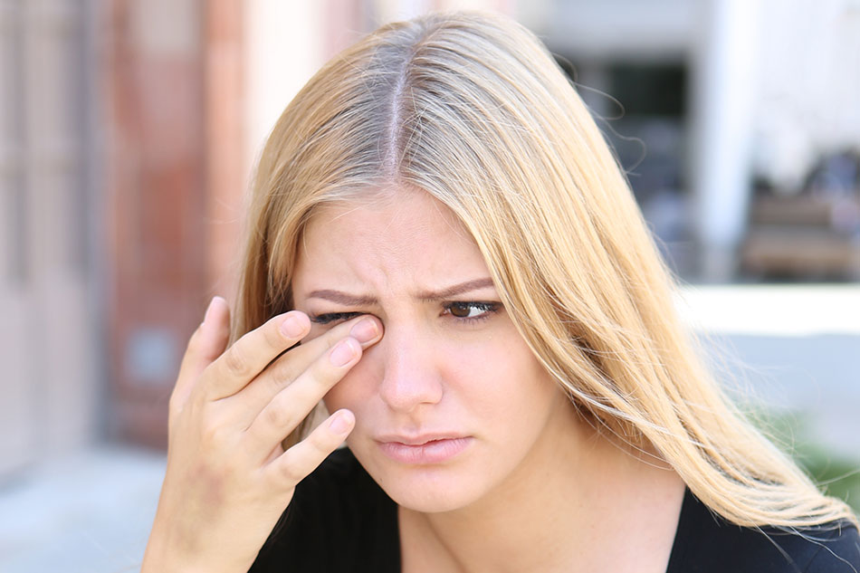 blonde woman rubbing irritated right eye