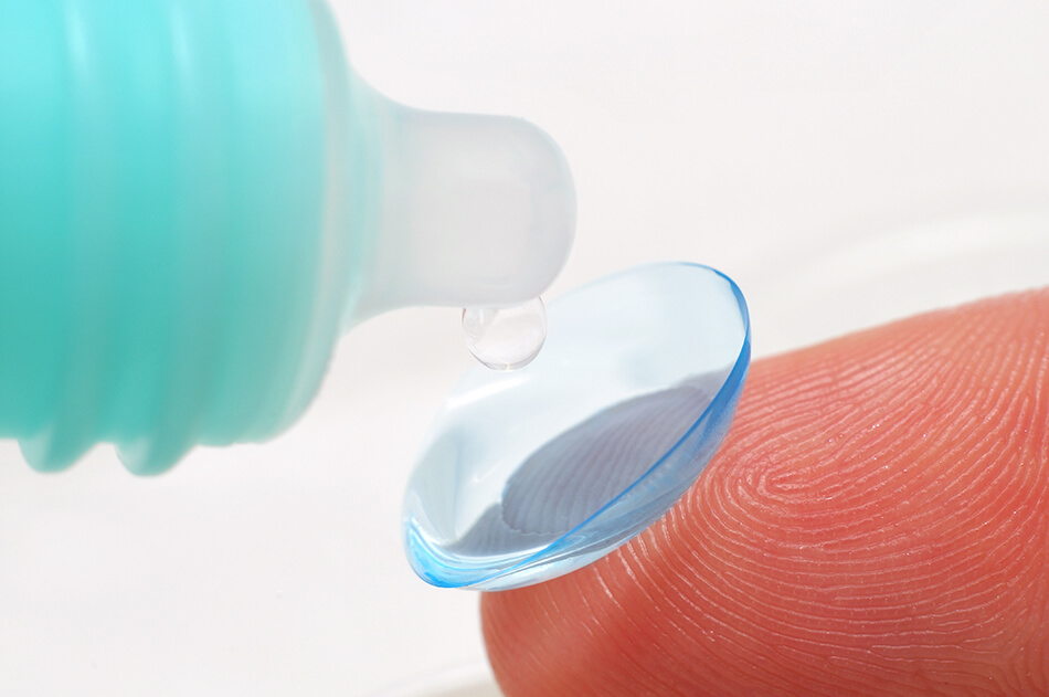 close-up of finger holding contact lens and contact lens solution bottle and drop