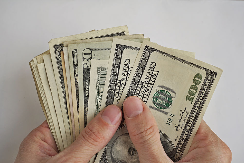 man’s hands holding several 20 and 100 dollar bills