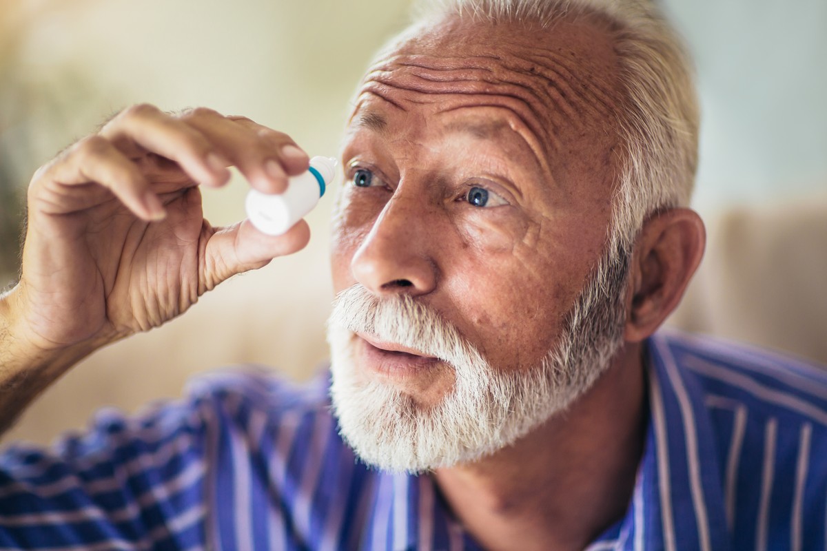 older man putting eye drops in right eye