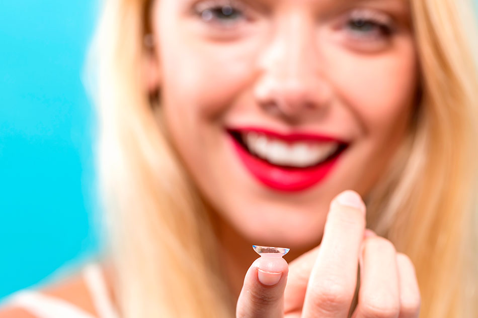 Smiling young woman offering a contact lens on her finger