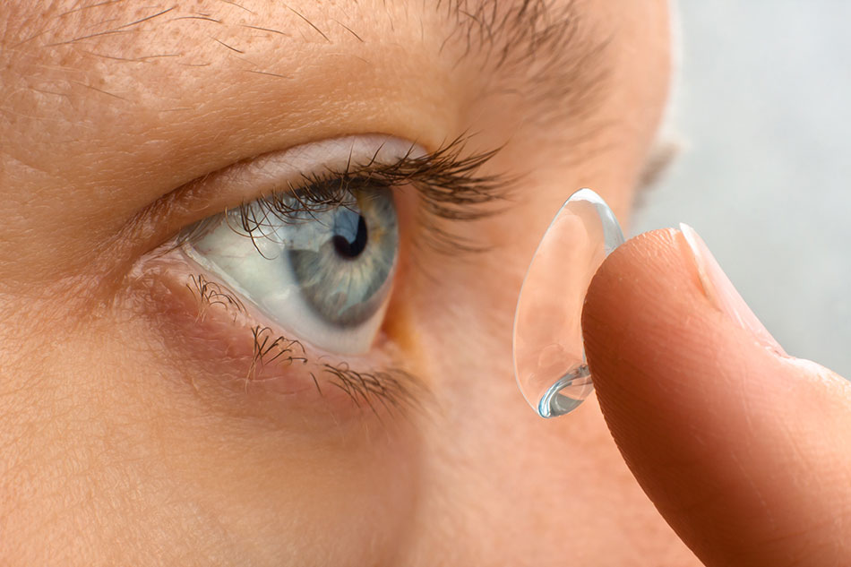 woman holding contact on finger up to her eye