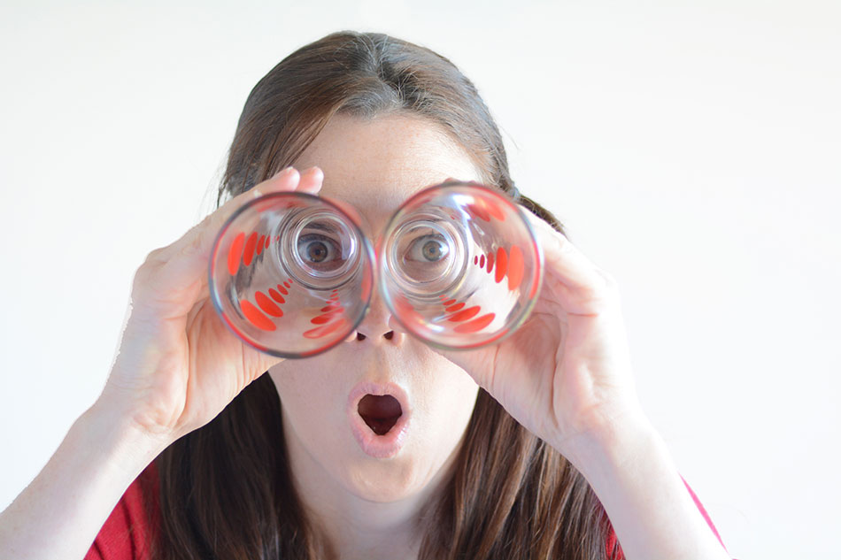 Woman looking through the bottom of drinking glasses with a surprised look on her face