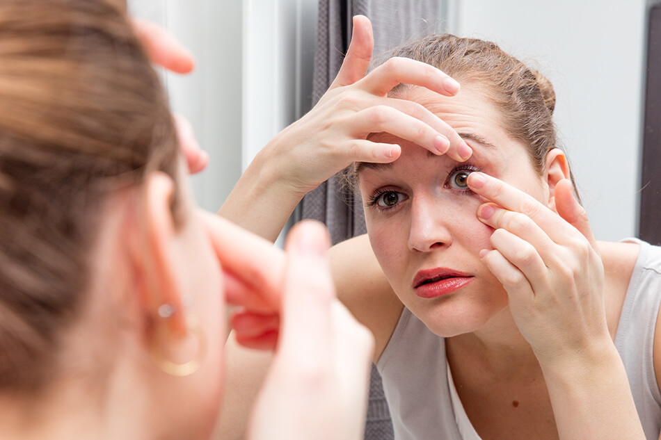 woman putting contact lens in right eye in the mirror