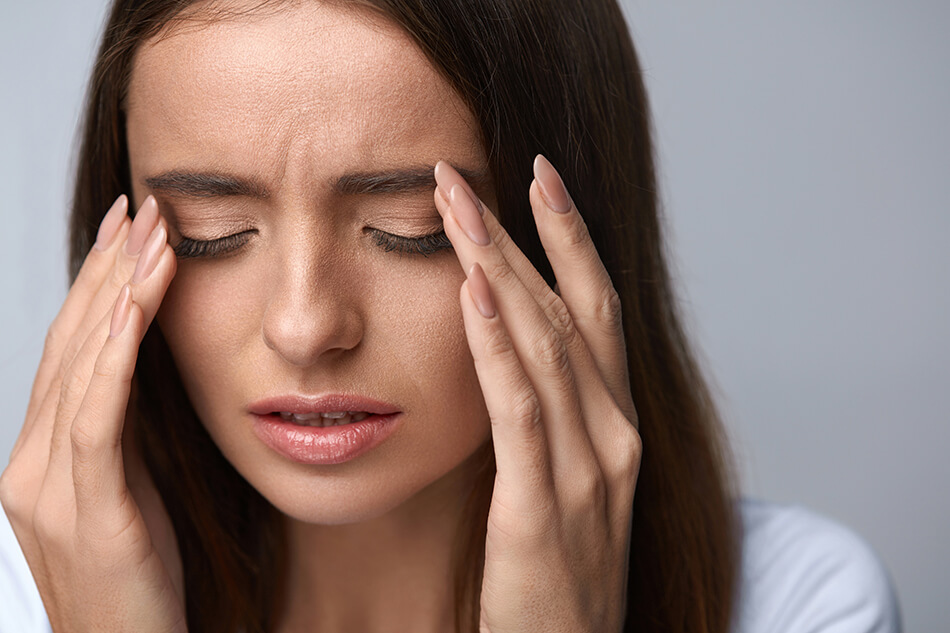 woman rubbing eyes on plain gray background