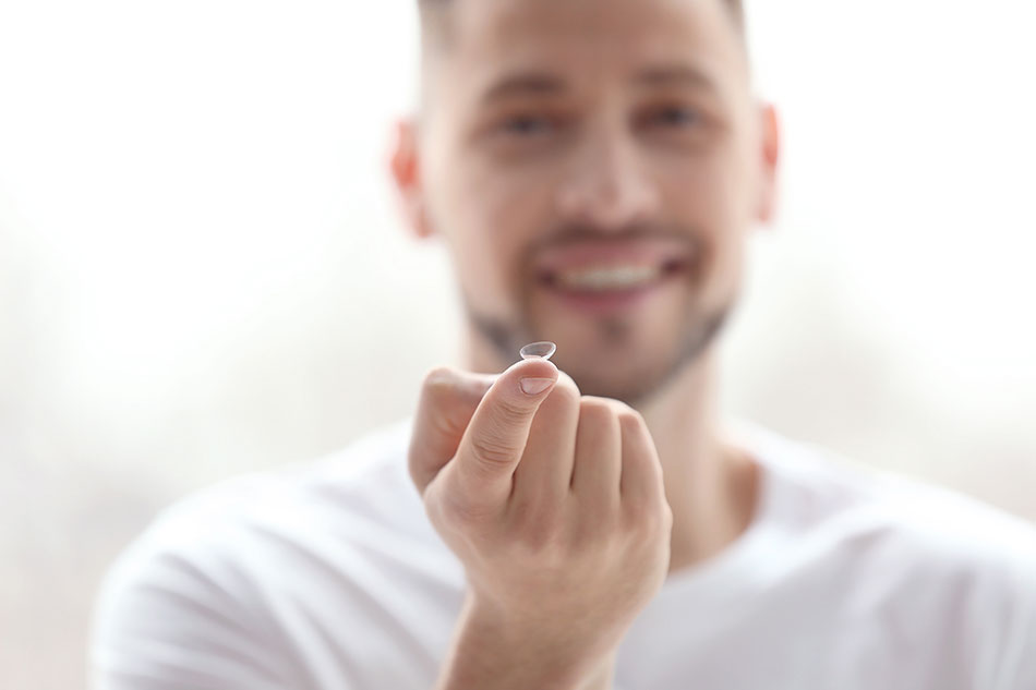 Smiling young man with contact lens on the tip of his finger pointed up